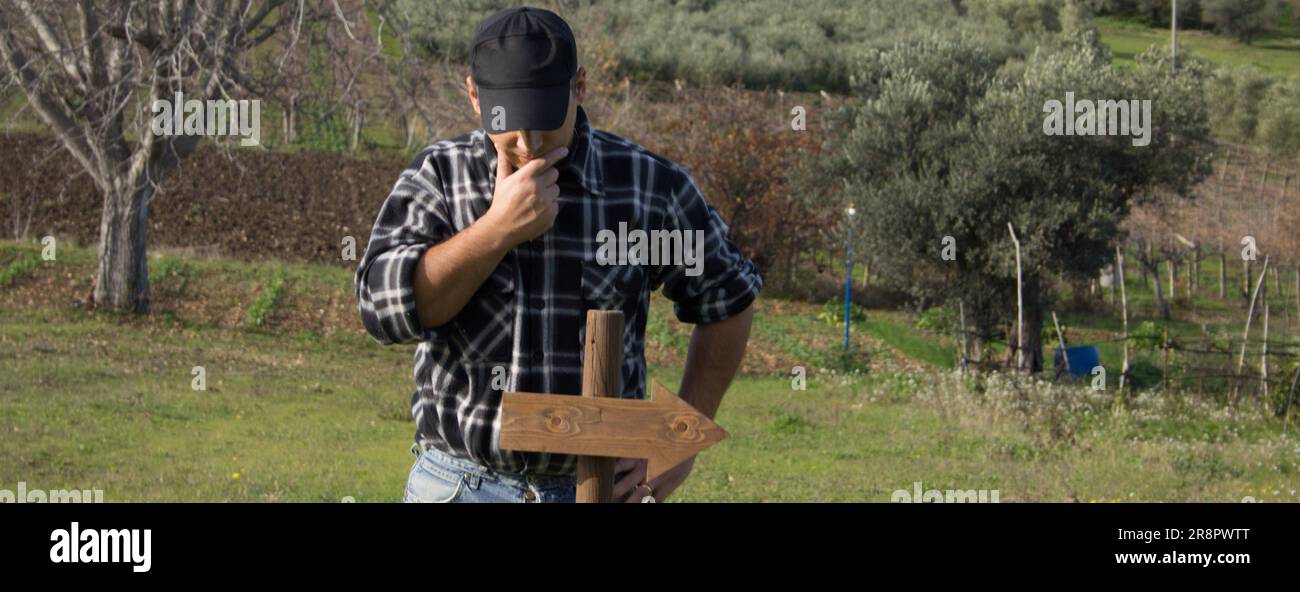 Image d'un homme perplexe regardant un poteau avec une flèche indiquant la direction. Homme qui a perdu son chemin. Bannière horizontale Banque D'Images