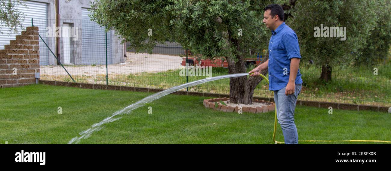 Image d'un homme arroser son jardin avec un tuyau. Entretien et entretien des pelouses et référence aux déchets d'eau et à la sécheresse. Bannière horizontale Banque D'Images