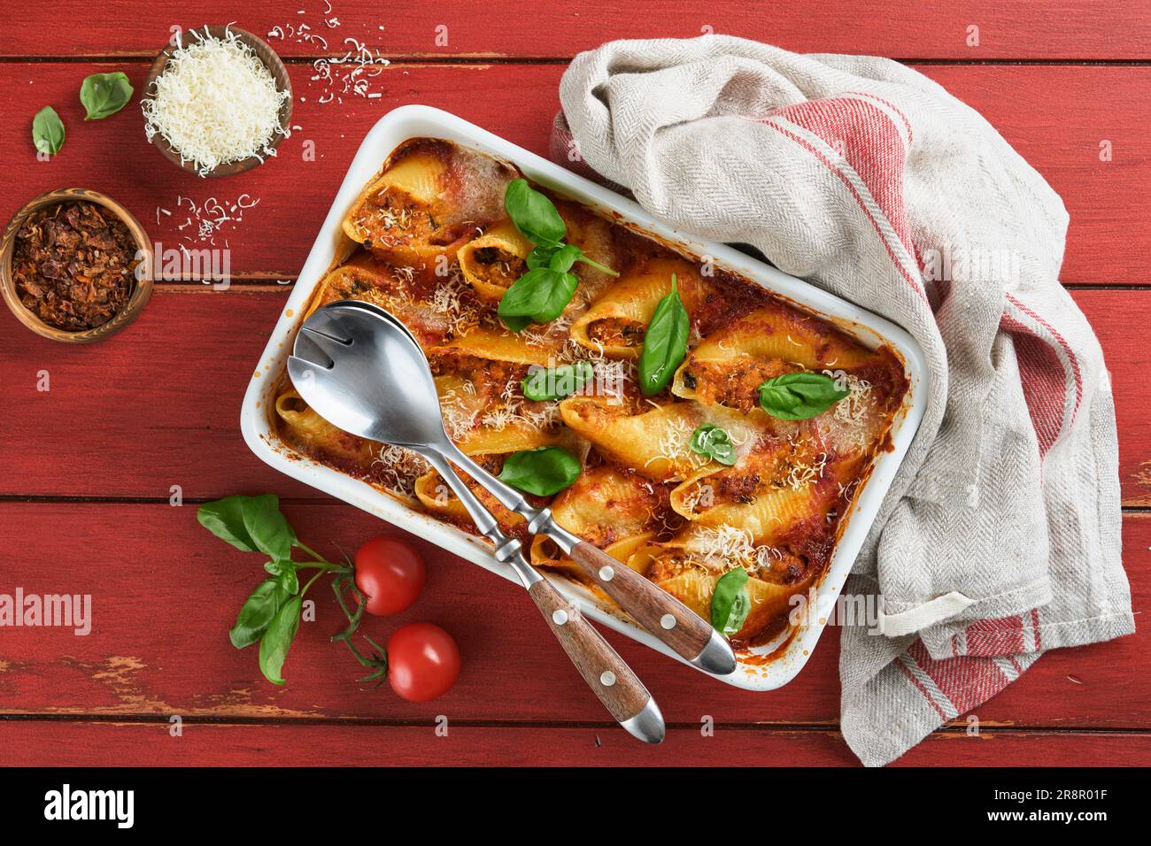 Cannelloni ou conchiglioni. Pâtes farcies cuites à la sauce à la viande bolognaise, tomates, basilic sur une table rustique en bois rouge. Bolo italien traditionnel Banque D'Images