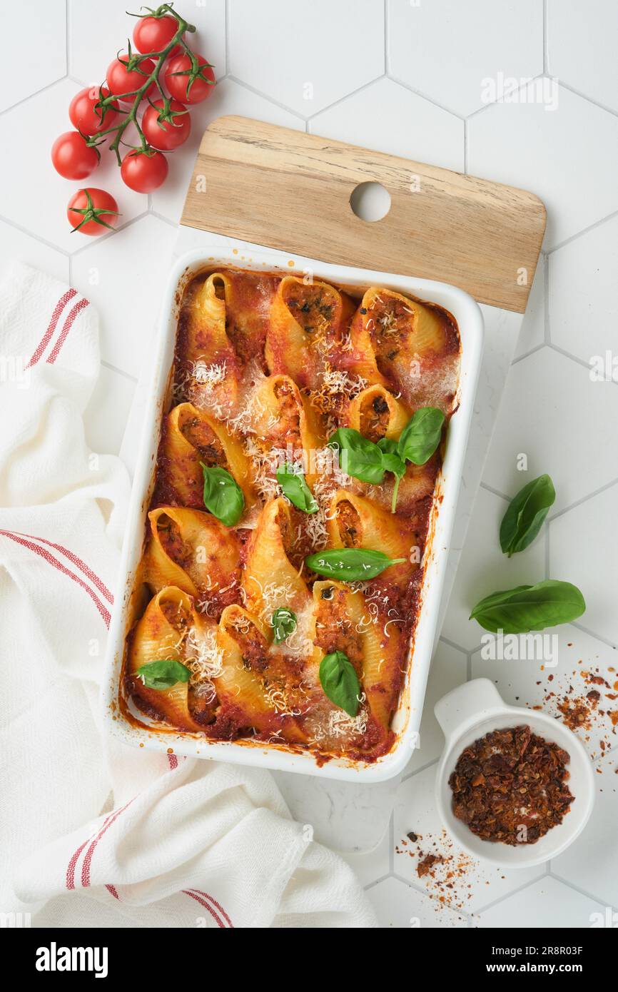 Cannelloni ou conchiglioni. Pâtes farcies cuites au four avec sauce à la viande bolognaise, tomates, basilic sur table moderne en carreaux blancs. Bolo italien traditionnel Banque D'Images