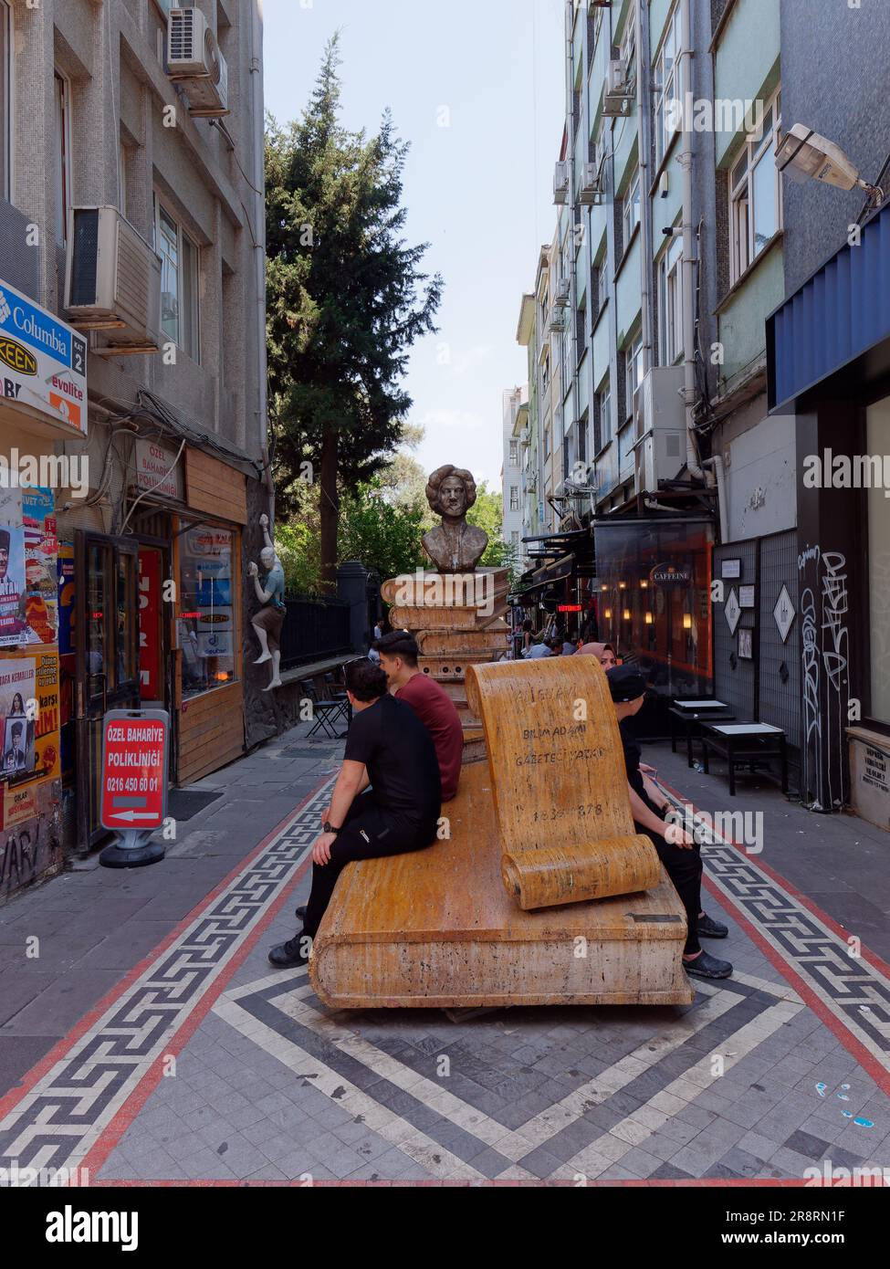 Les gens sont assis à côté d'une sculpture en bois et s'asseyent dans une rue étroite dans le quartier de Kadikoy sur le côté asiatique d'Istanbul, en Turquie. 22 juin 2023 Banque D'Images