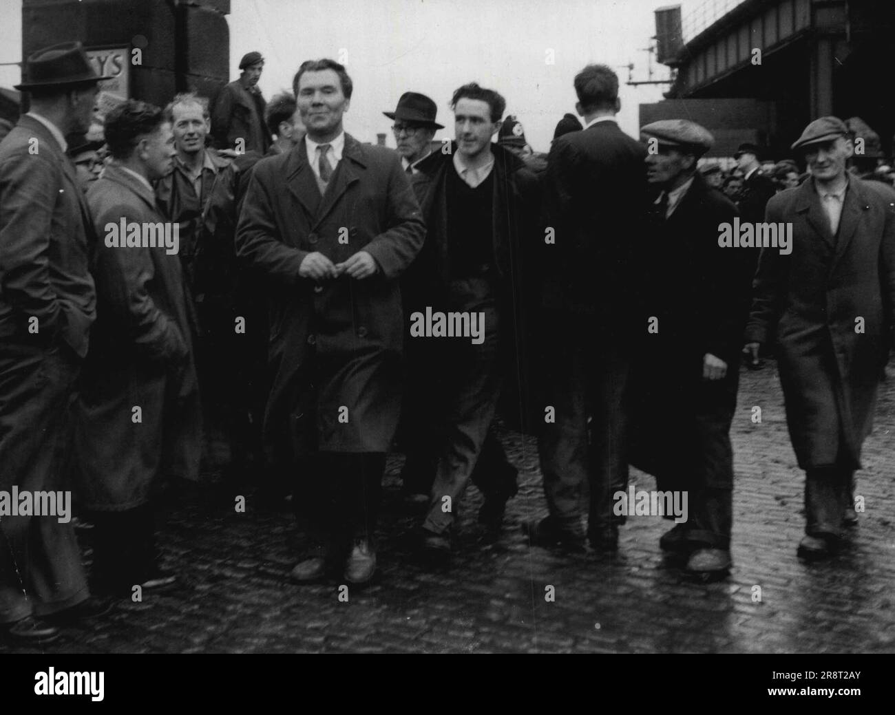 Il dirige le « travail en mouvement » -- Bob Crosbie, 46 ans (en imperméable boutonné, au centre), se rapporte au travail au Gladstone Dock, Liverpool, après avoir de nouveau persuadé ses adeptes au quai de ne pas frapper. Une police supplémentaire avait été rédigée au Gladstone Dock pour retenir plus de 1 000 grévistes qui ont essayé de bloquer les tarifs des quais. 20 octobre 1954. (Photo par Daily Mirror). Banque D'Images