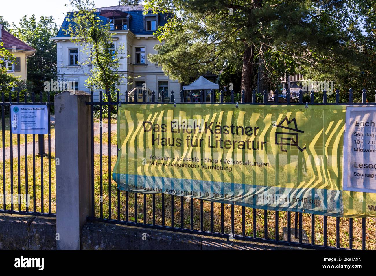 Une bannière sur la clôture en fer forgé du jardin fait la promotion de la Maison Erich Kästner pour la littérature à la Villa Augustin, Antonstraße 1, Dresde, Saxe, Allemagne. L'oncle d'Erich Kästner, Franz Augustin, a acheté la villa néo-classique tardive en 1915. Depuis 2000, elle abrite un musée, un café de lecture et des espaces événementiels dédiés à la vie et à l'œuvre de l'écrivain né à Dresde. Banque D'Images