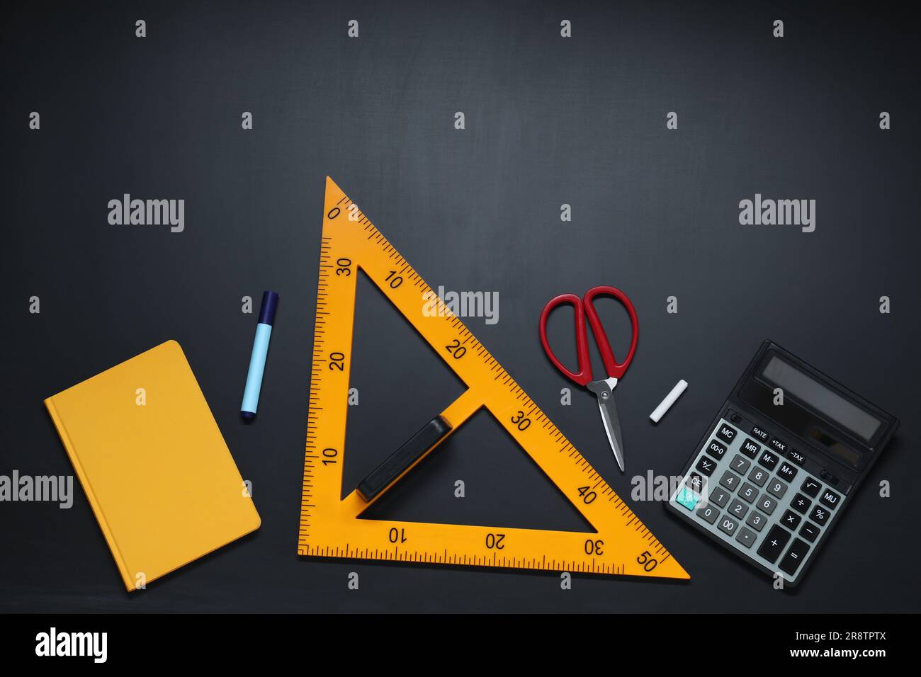 Règle triangulaire, ciseaux, craie, calculatrice, marqueur et carnet sur table noire, plat Banque D'Images