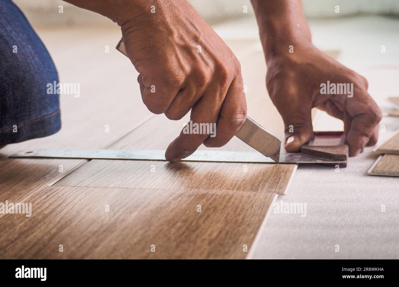 Un technicien coupe les carreaux de vinyle de luxe avec un couteau pour poser le sol avant du placer sur la mousse de nivellement. Banque D'Images
