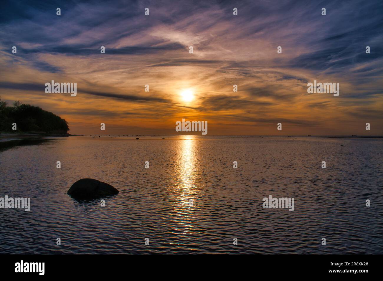 Coucher de soleil, petits rochers dans l'eau à la rive. Ondes lumineuses. Île de Poel sur la mer Baltique. Photo de la nature de la côte Banque D'Images