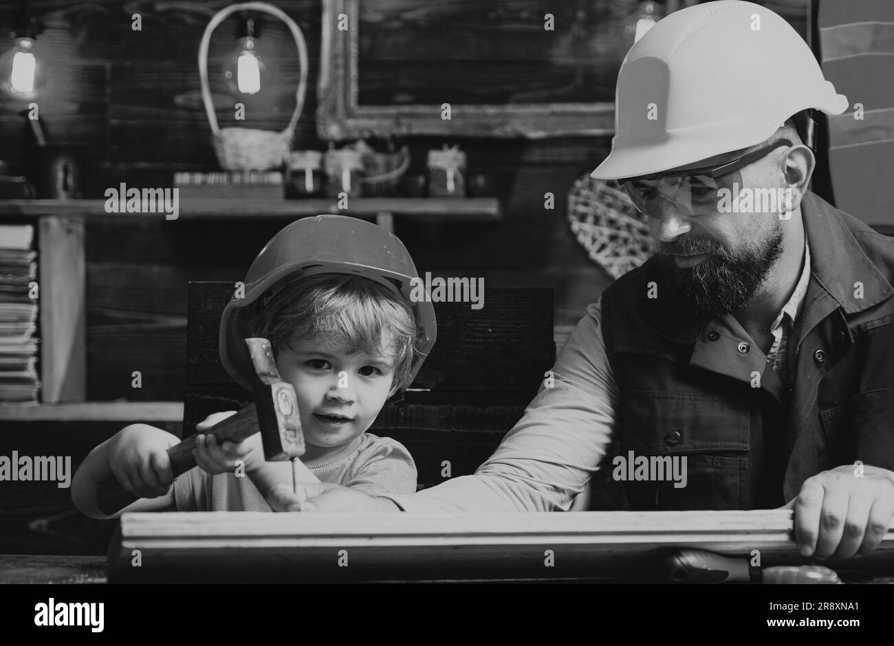 Mignon petit fils et père dans un chapeau rigide tenant une planche en bois et un marteau. Garçon aidant son père à la maison Banque D'Images