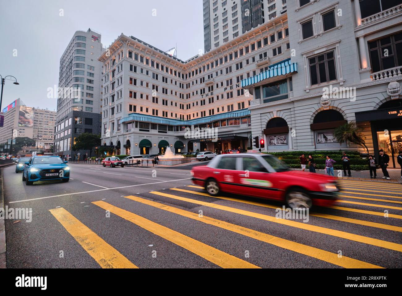 Hong Kong, Chine - avril 24 2023 : l'hôtel Peninsula et le taxi rouge sur les bandes jaunes de croisement Banque D'Images