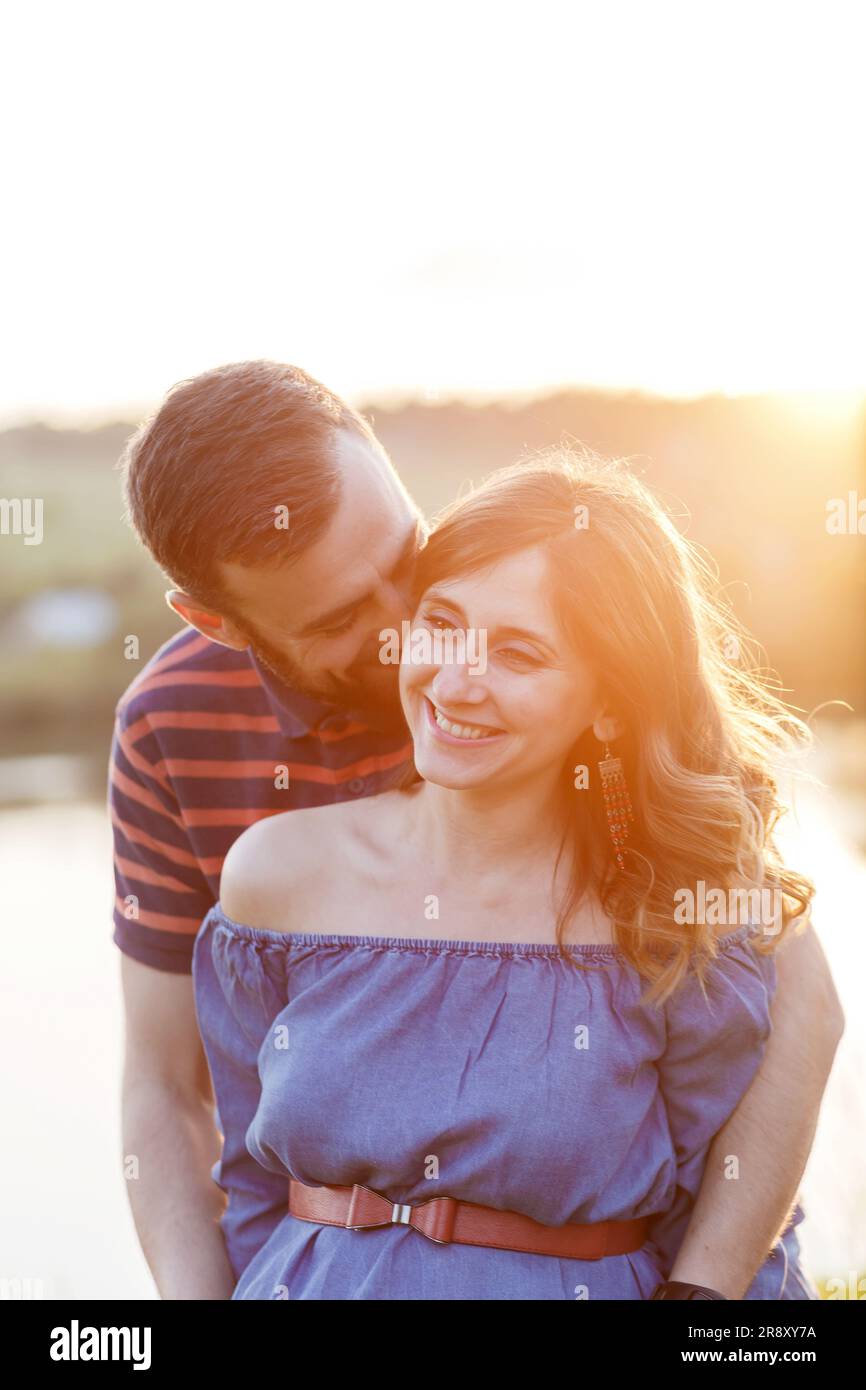 l'homme et la femme enceinte en robe s'embrasent en été au coucher du soleil Banque D'Images
