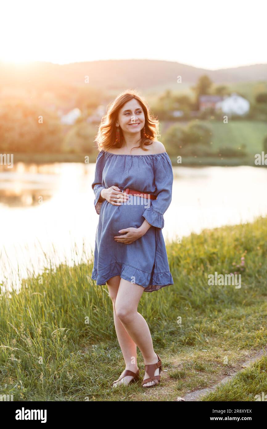 femme enceinte en robe bleue tient son ventre sous les rayons du soleil Banque D'Images