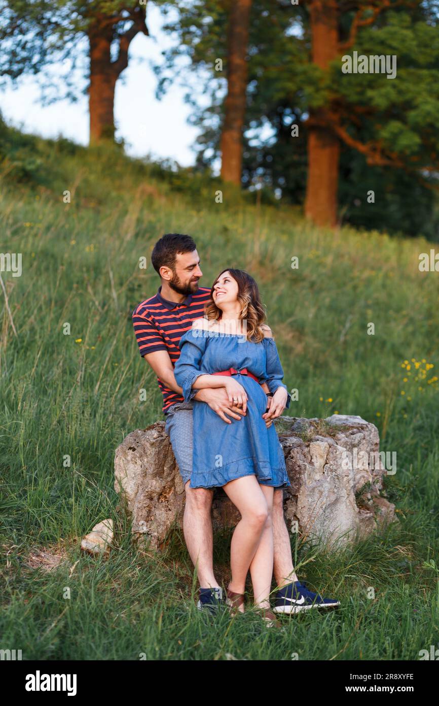 l'homme et la femme enceinte en robe s'embrasent en été au coucher du soleil Banque D'Images