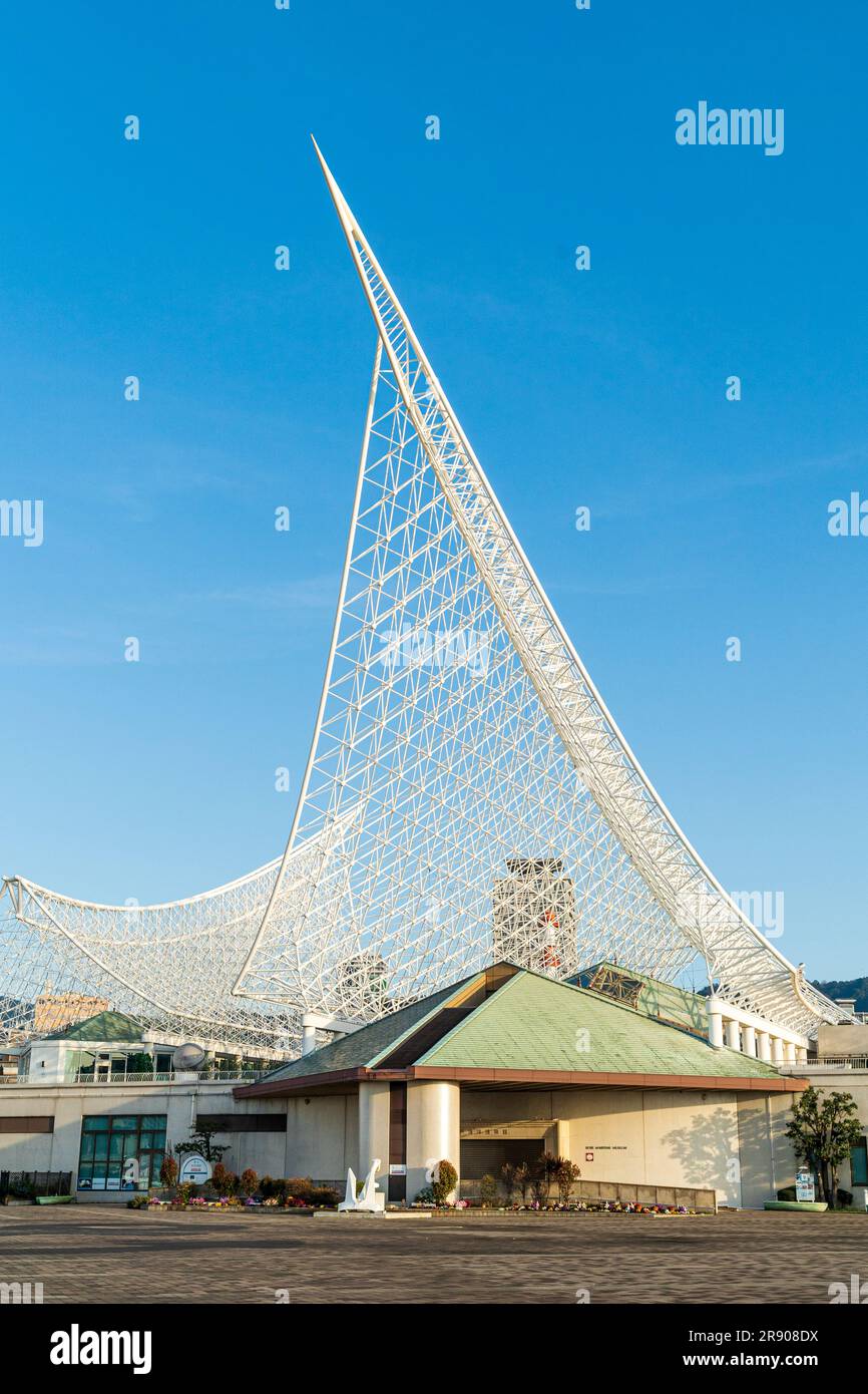 L'entrée et la façade du musée maritime de Kobe avec son cadre en métal blanc incliné au-dessus de la structure ressemblant à la coque d'un navire contre un ciel bleu de l'aube. Banque D'Images