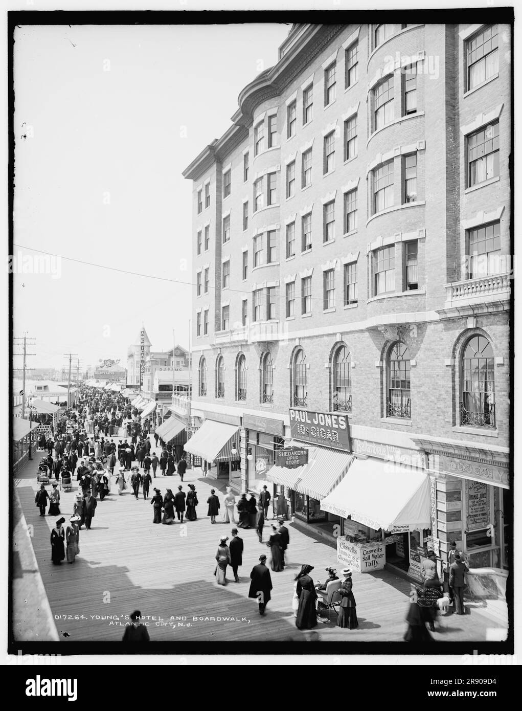 Young's Hotel and BoardWalk, Atlantic City, N.J., c1904. Magasins et pharmacies vendant: Jus d'orange de 'shinn, taffy d'eau salée de Caswell, bonbons à mâcher "immense", soda de crème glacée, penochis mexicain, chocolat chaud, Eau de Lithia de Ballardvale, 10c cigares, type étain. Au loin se trouvent le jardin américain et les bains Brady. Les gens sont poussés dans les chaises de bain. Banque D'Images