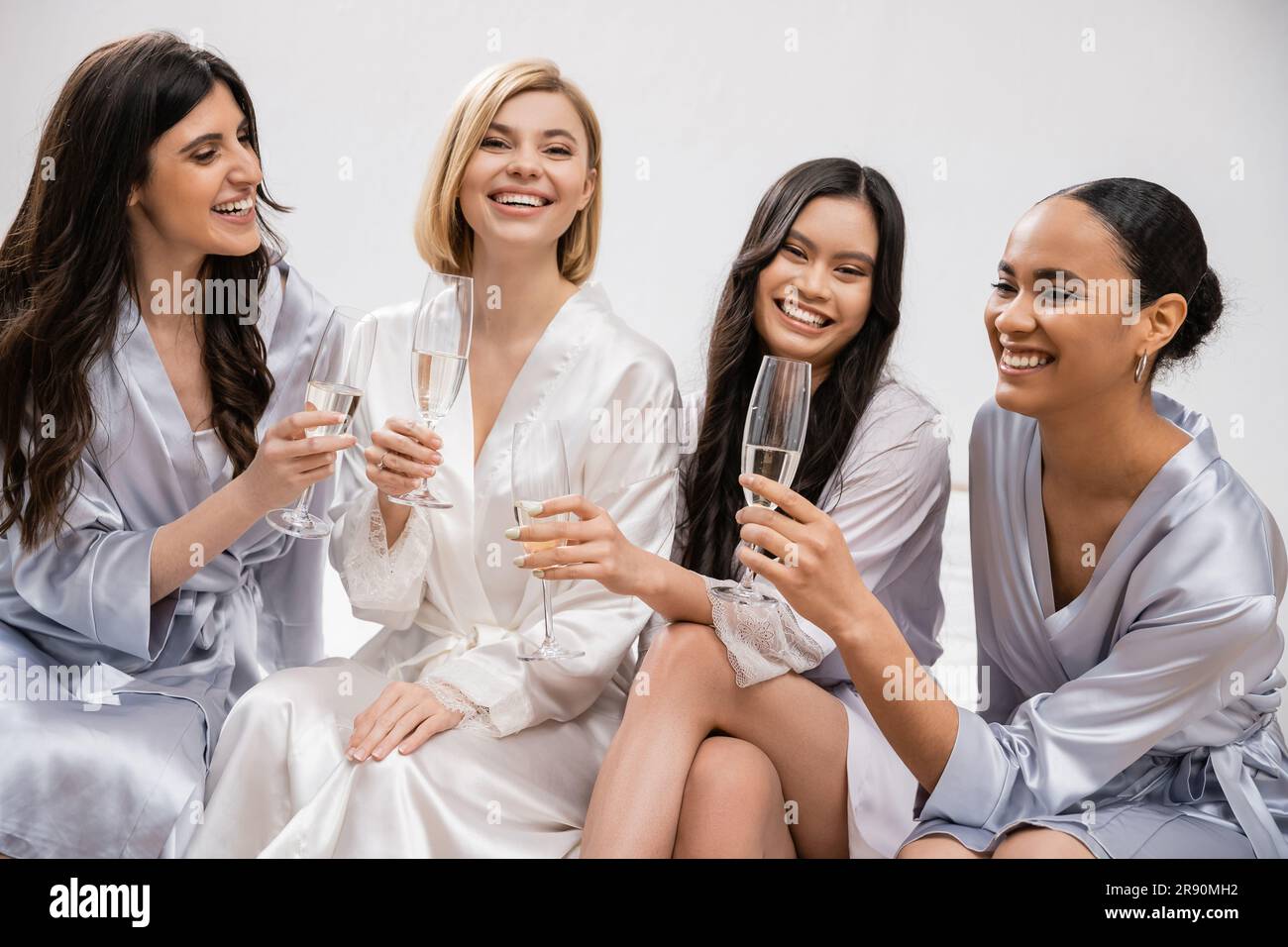 fête de mariée, amies interraciales tenant des verres de champagne, célébration avant le mariage, femmes brunes et blondes, mariée et épouses demoiselles Banque D'Images