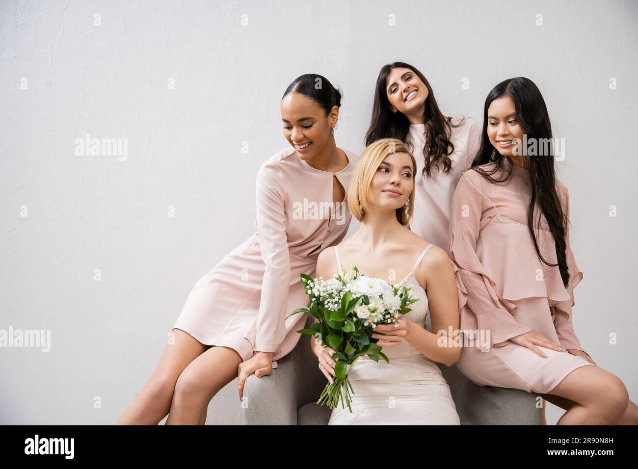 photographie de mariage, quatre femmes, mariée joyeuse et demoiselle mariée, amies interraciales, jour de mariage, diversité culturelle, assis sur un fauteuil, bac gris Banque D'Images
