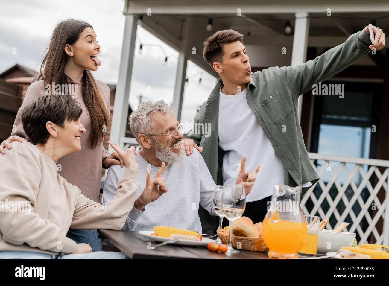 Un jeune homme qui colle à la langue tout en emportant un selfie avec sa sœur et ses parents d'âge moyen joyeux lors d'une fête barbecue et de la fête des parents à backyar Banque D'Images