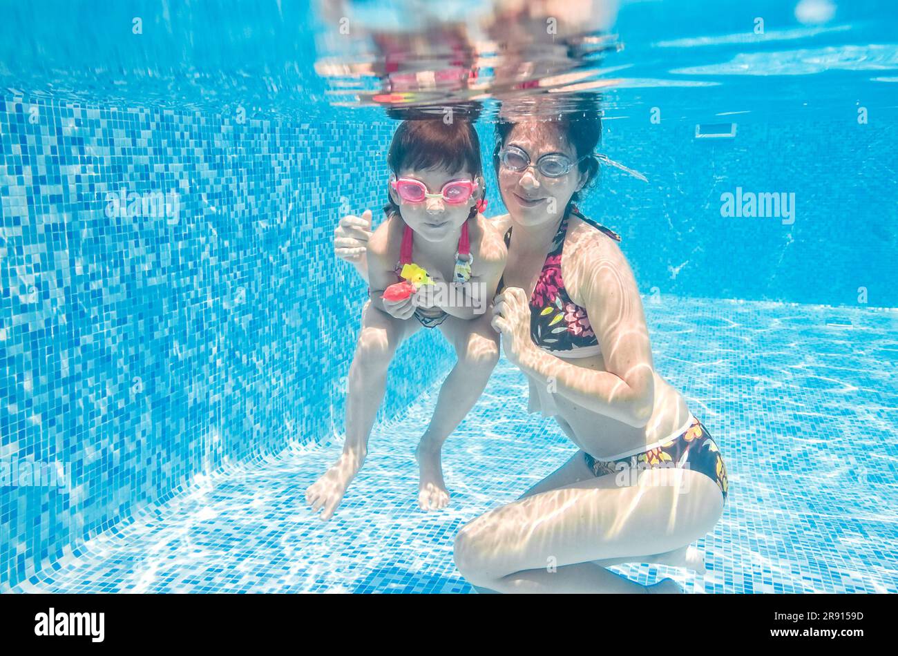 Famille nage dans la piscine sous l'eau, mère active heureuse et enfant s'amusent sous l'eau, fitness et sport avec enfant en vacances d'été sur la station Banque D'Images