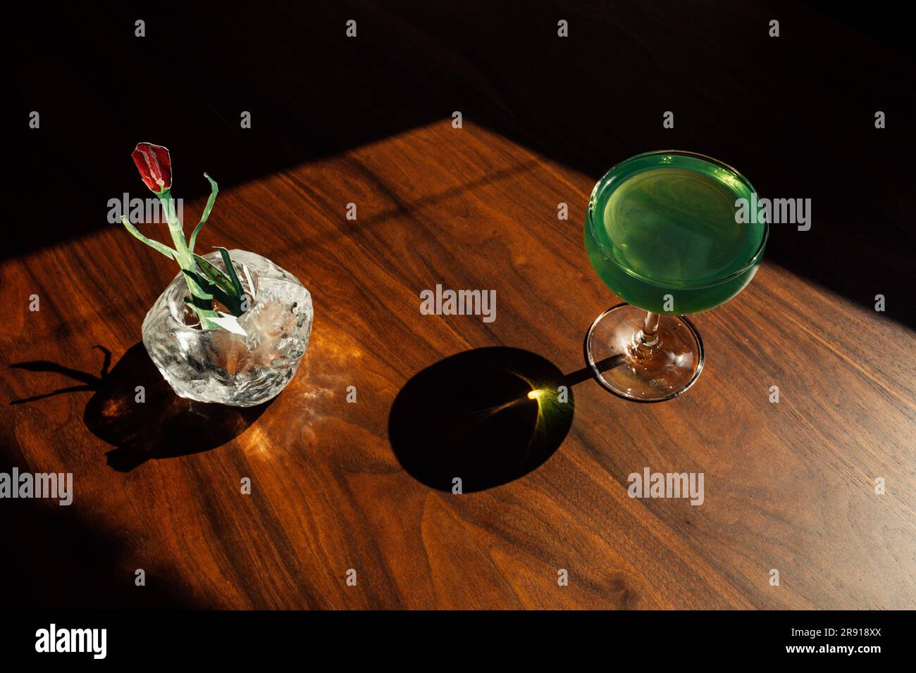 tulipe en papier dans un vase avec une boisson à l'absinthe verte, cocktail sur une table en bois au soleil avec des ombres dures Banque D'Images