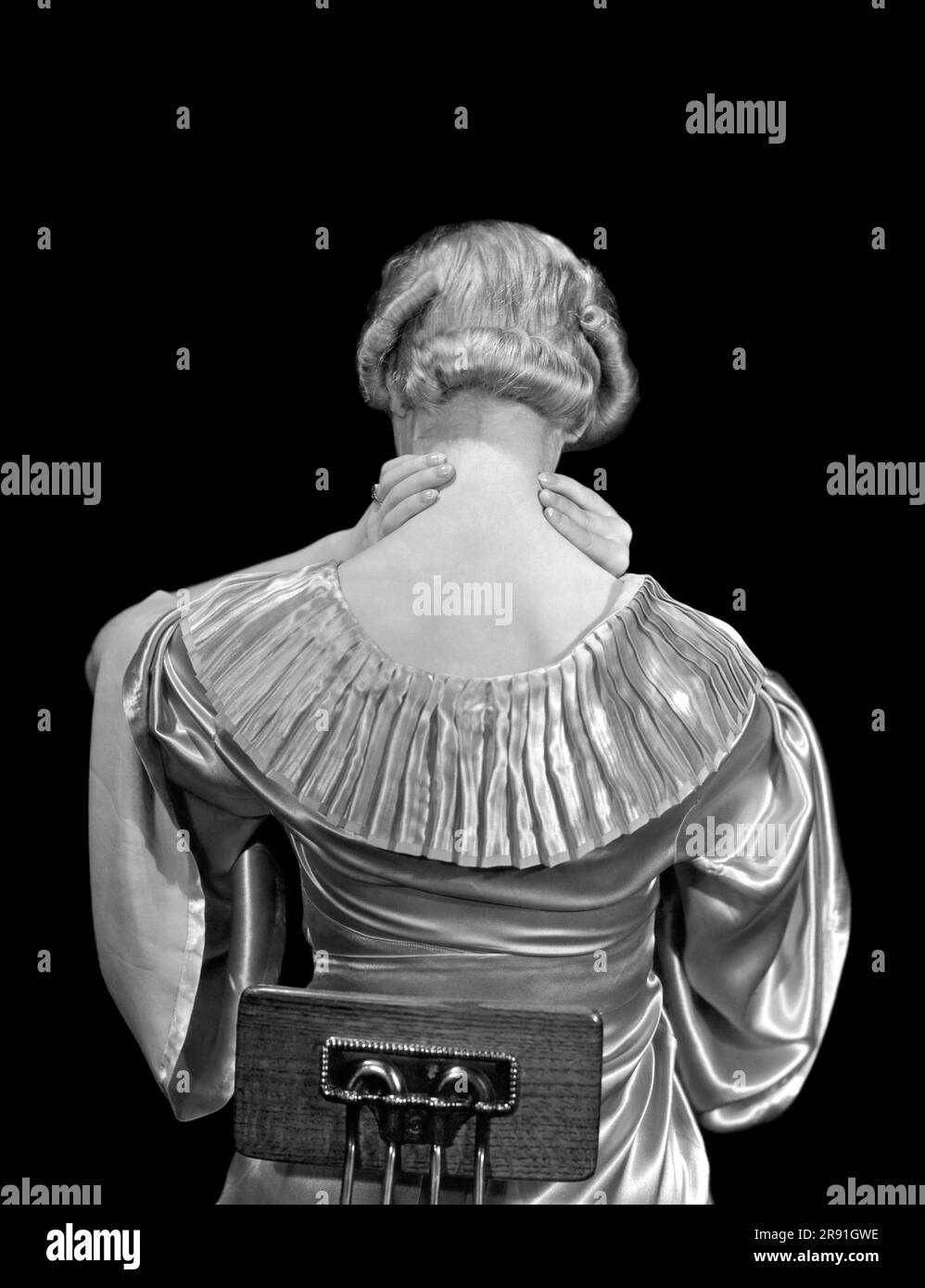 États-Unis : c. 1930. Une femme assise sur une chaise se moque de l'arrière de son cou. Banque D'Images