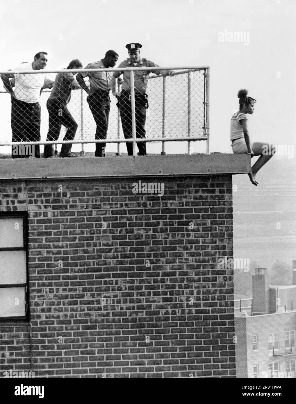 New York, New York: Juin 1972 la police de New York tente de paraître inchalante en essayant de parler à une jeune femme de ne pas sauter du rebord de 15th étages sur lequel elle est perchée. Banque D'Images