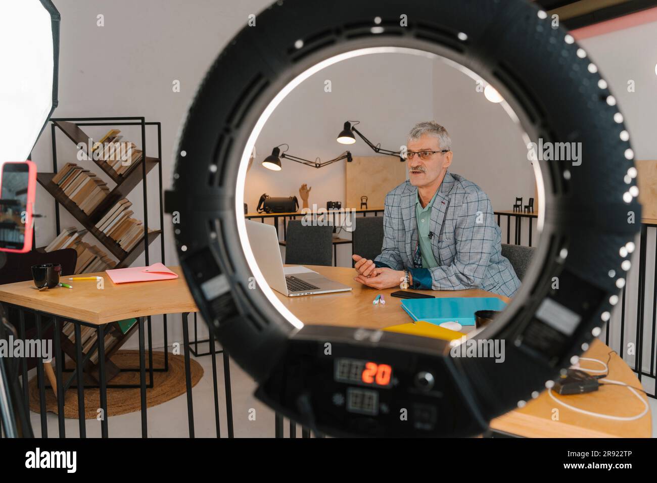 Homme d'affaires enregistrant des cours en ligne dans un studio vu à travers la lumière d'anneau Banque D'Images