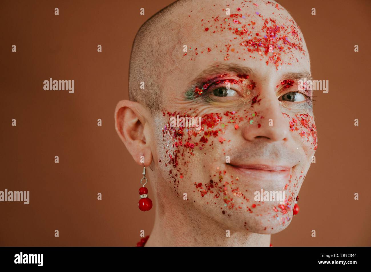 Visage souriant de la reine de drag avec paillettes rouges sur le visage sur fond marron Banque D'Images