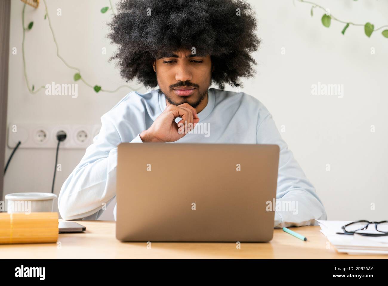 Homme d'affaires attentionné avec main sur le menton travaillant sur un ordinateur portable à la maison Banque D'Images