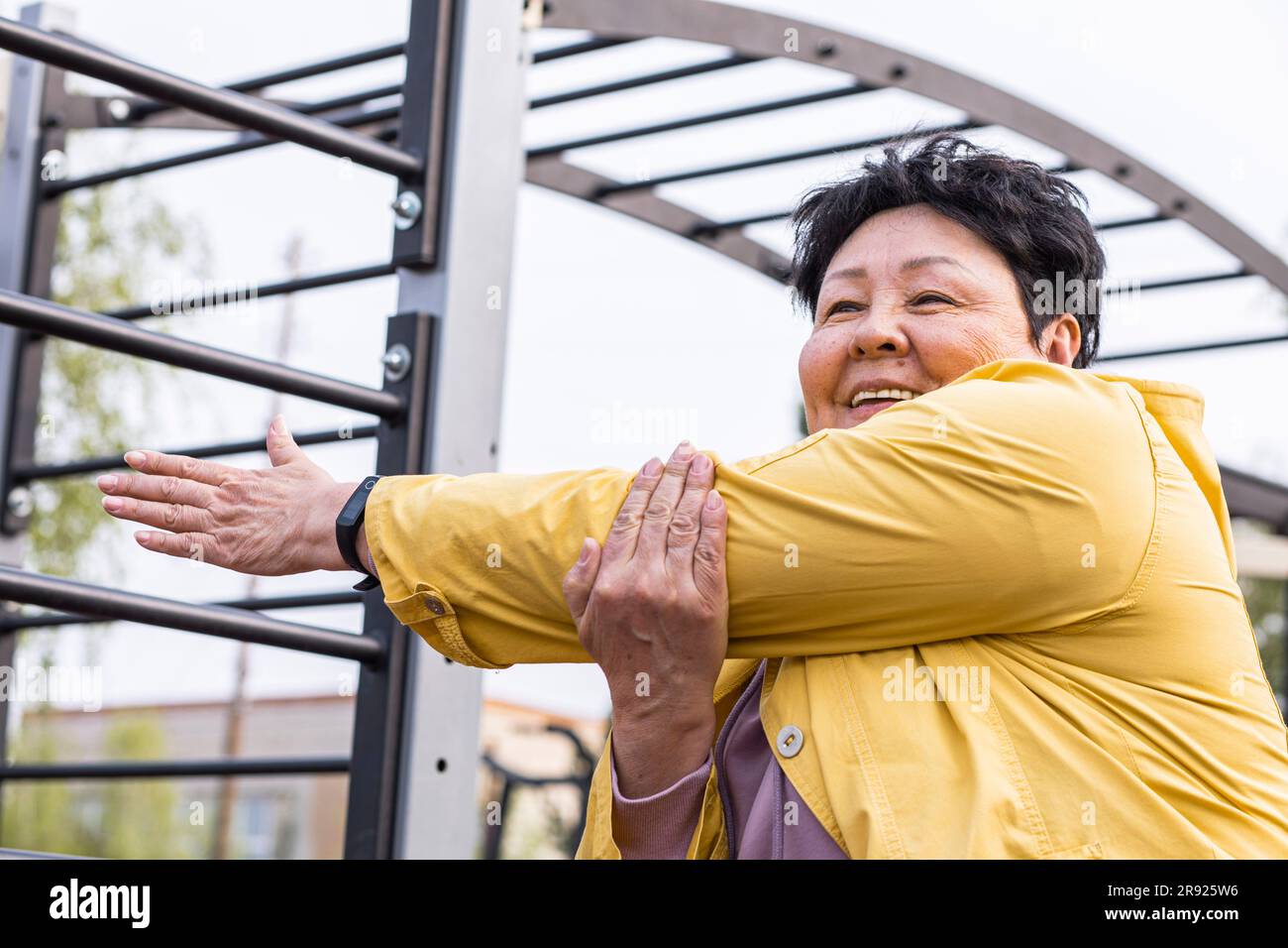 Femme aînée souriante faisant de l'exercice d'échauffement au parc Banque D'Images