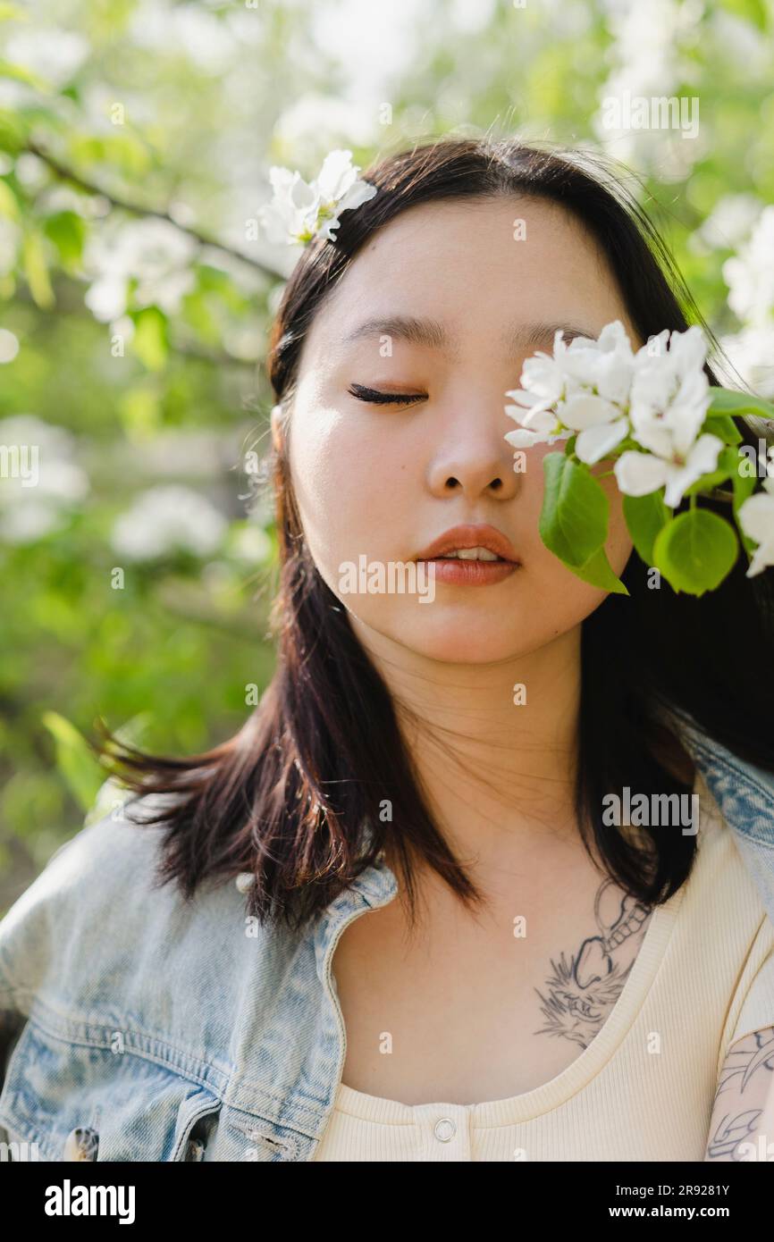 Jeune femme avec les yeux fermés par des fleurs blanches sur la branche Banque D'Images
