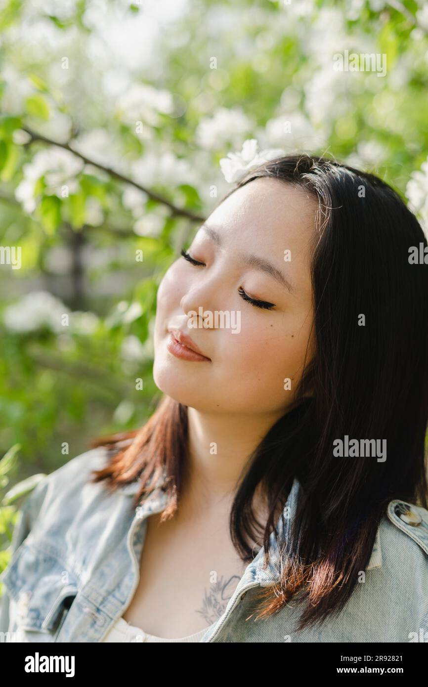 Jeune femme avec les yeux fermés par arbre à fleurs Banque D'Images