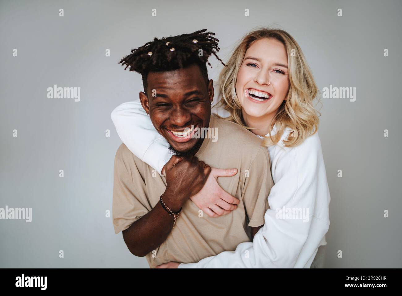 Jeune couple joyeux avec le bras autour de rire sur fond gris Banque D'Images