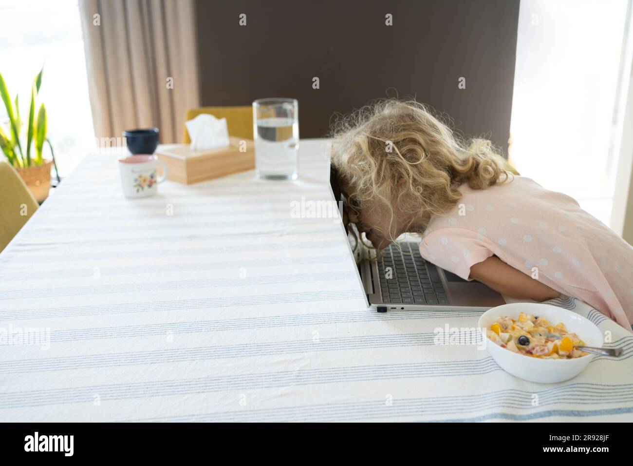 Une fille se penchait sur un ordinateur portable avec un bol de petit déjeuner sur une table à la maison Banque D'Images