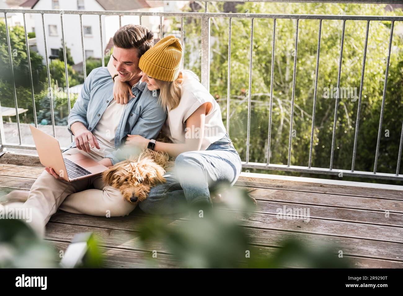 Couple heureux utilisant un ordinateur portable avec chien sur le balcon Banque D'Images
