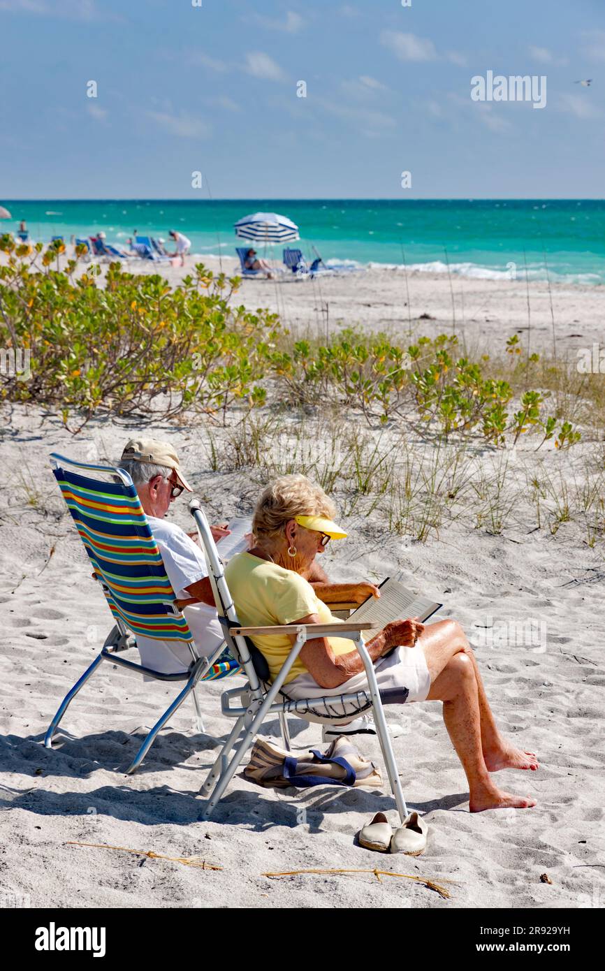 Couple senior retraité lisant sur la plage de Siesta Key, Sarasota, la côte ouest ou du golfe de Floride, États-Unis. Banque D'Images