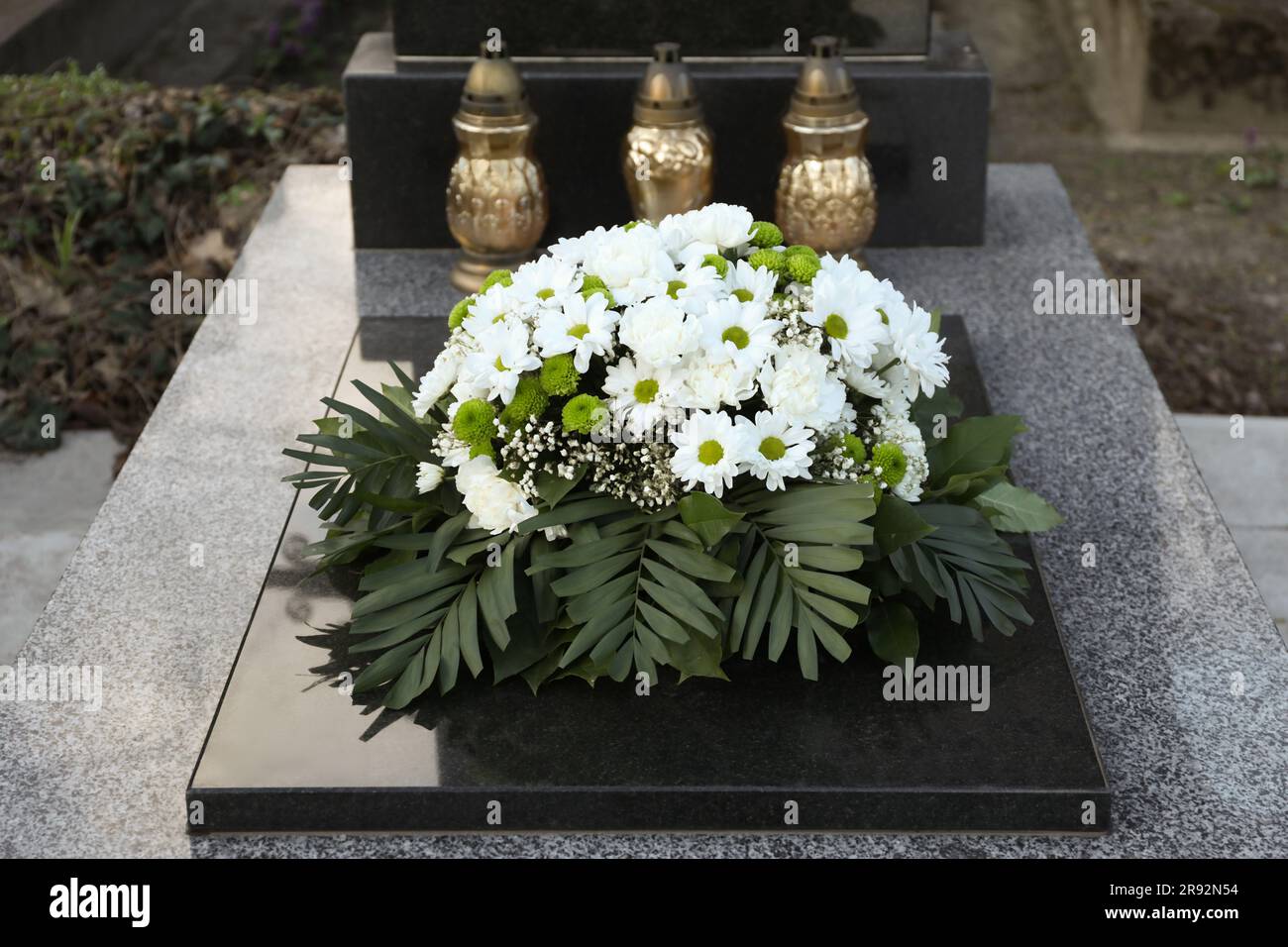Couronne funéraire de fleurs et lanternes sur pierre tombale de granit dans le cimetière Banque D'Images