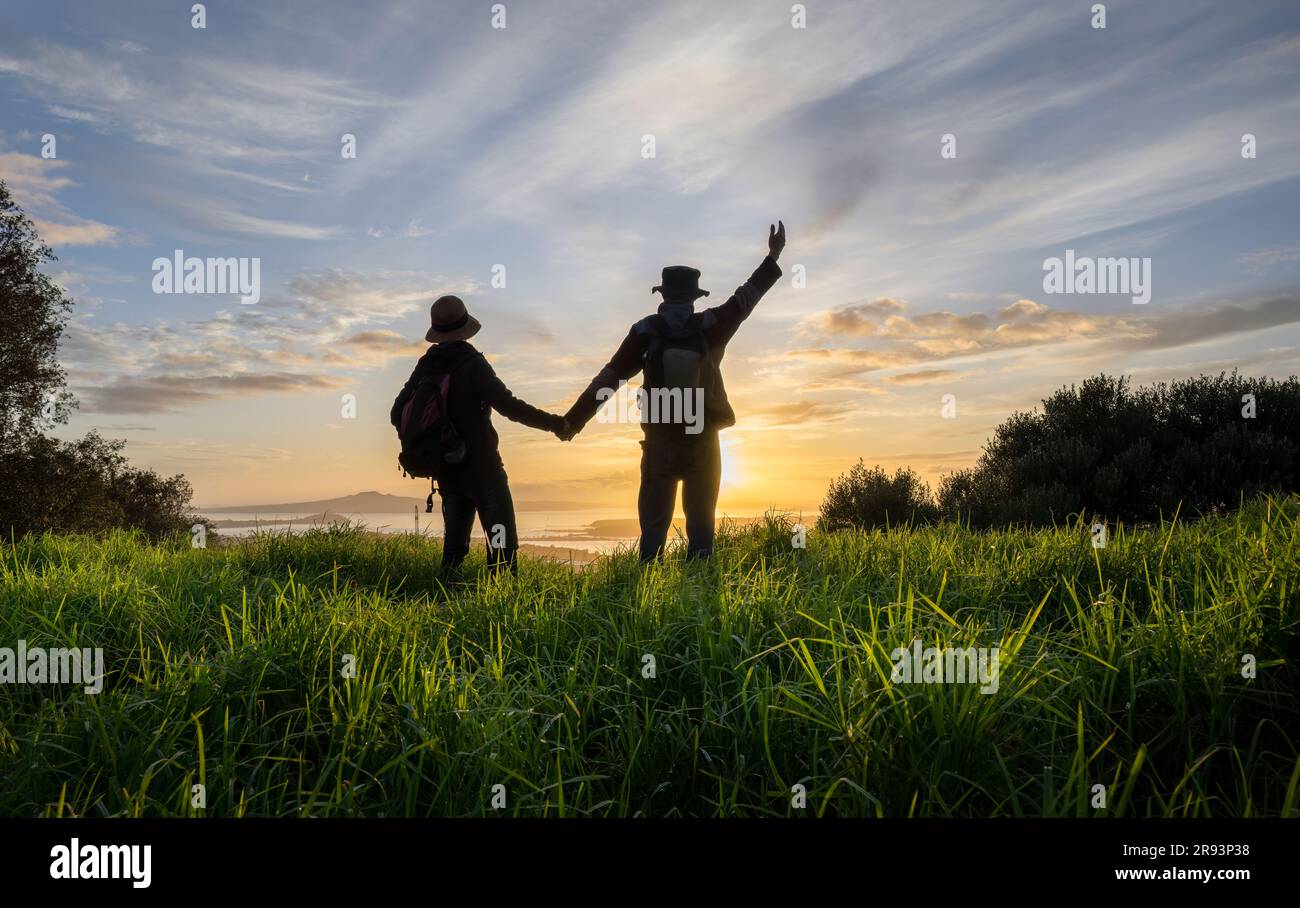 Couple tenant la main et debout sur le sommet de Mt Eden au lever du soleil. Rangitoto Island au loin. Auckland. Banque D'Images
