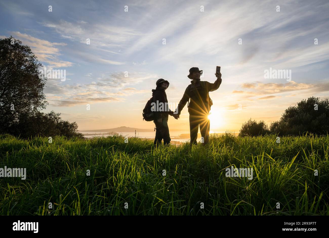 Couple debout sur le sommet du Mont Eden et prenant photo du selfie avec un smartphone au lever du soleil. Rangitoto Island au loin. Auckland. Banque D'Images