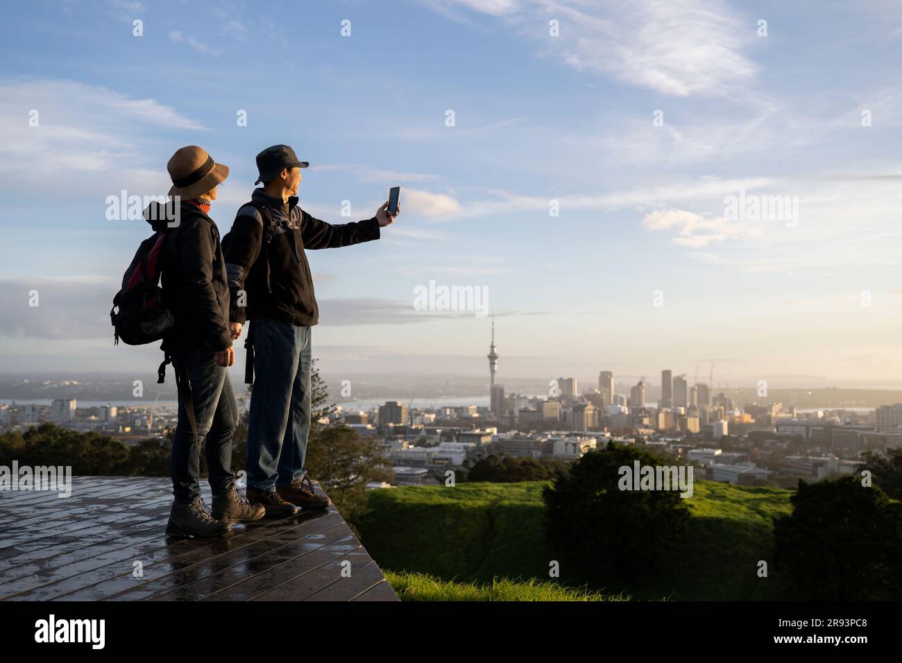 Couple prenant des photos avec un smartphone au sommet du Mont Eden au lever du soleil. Skytower en arrière-plan. Accent sélectif sur les personnes au premier plan. Auckland. Banque D'Images