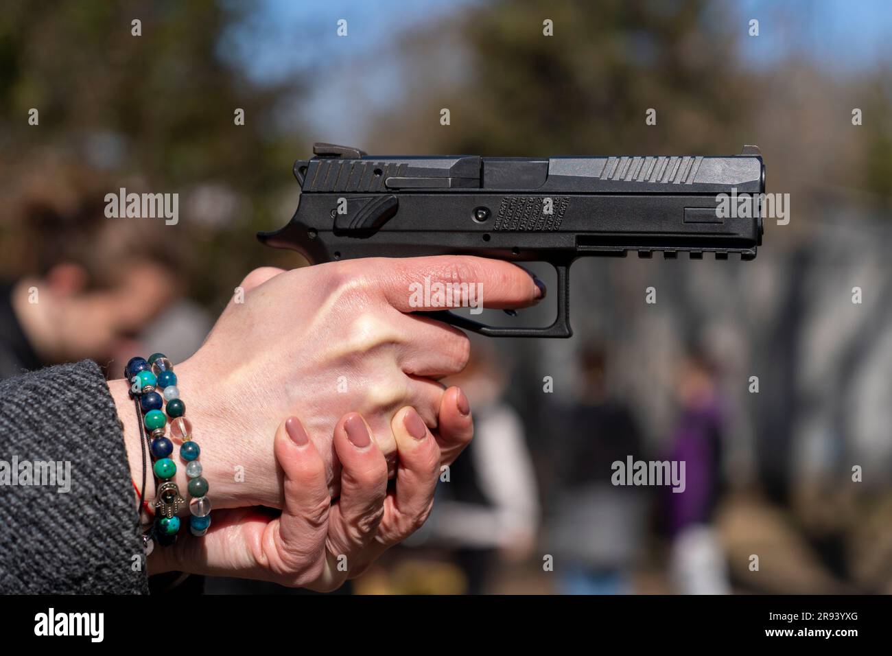 Main femelle avec bracelet tenant un pistolet automatique noir Banque D'Images