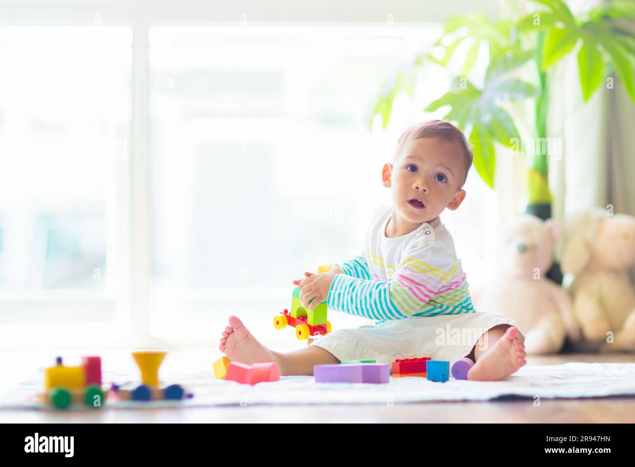 Adorable bébé asiatique apprenant à ramper et à jouer avec le jouet coloré de bloc dans la chambre blanche ensoleillée. Mignon rire enfant rampant sur un tapis de jeu. Banque D'Images