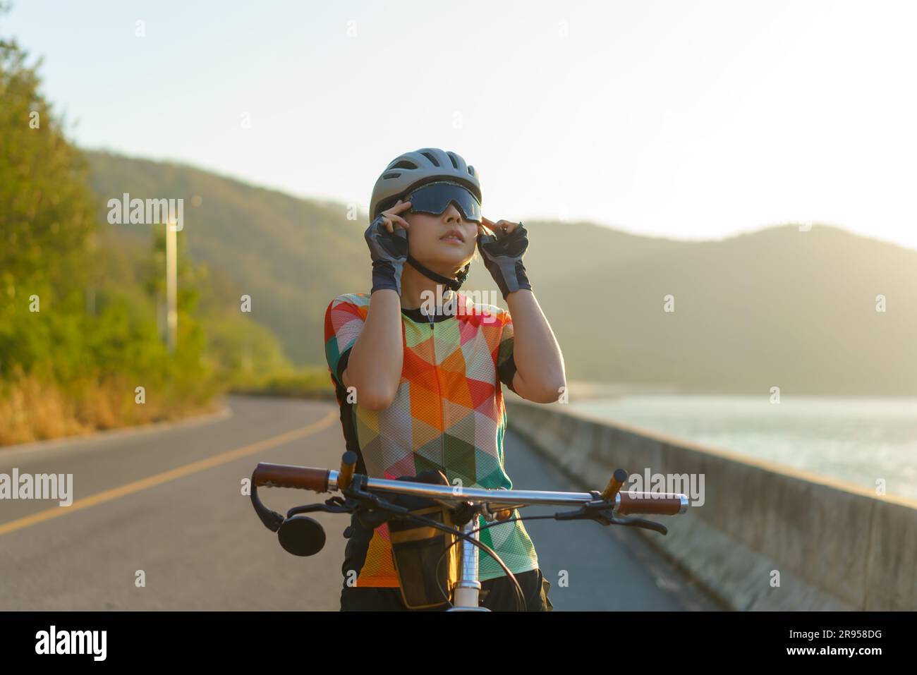 Femme cycliste asiatique portant des lunettes de soleil se préparer pour une promenade matinale en vélo autour du lac avec belle vue sur la montagne en arrière-plan. Banque D'Images