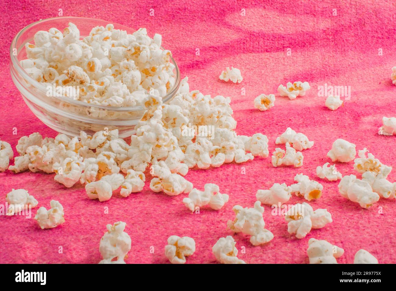 pop-corn dans une assiette en verre, sur fond rose inégal Banque D'Images