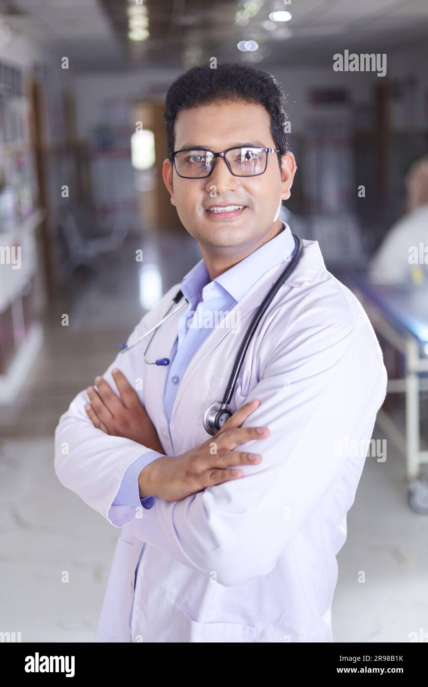 Portrait d'un jeune homme médecin en blouse blanche de laboratoire avec les bras croisés. Heureux médecin senior en manteau souriant sur fond de couloir d'hôpital. Banque D'Images