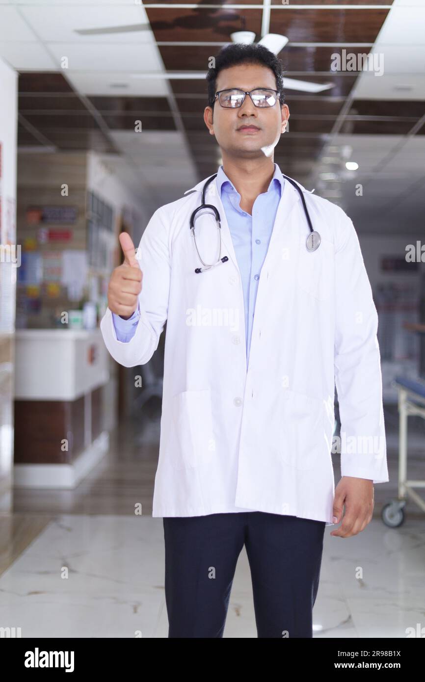 Portrait d'un jeune médecin montrant les pouces vers le haut. Heureux docteur senior en blouse blanche de laboratoire sur fond de couloir d'hôpital. confiance. Banque D'Images