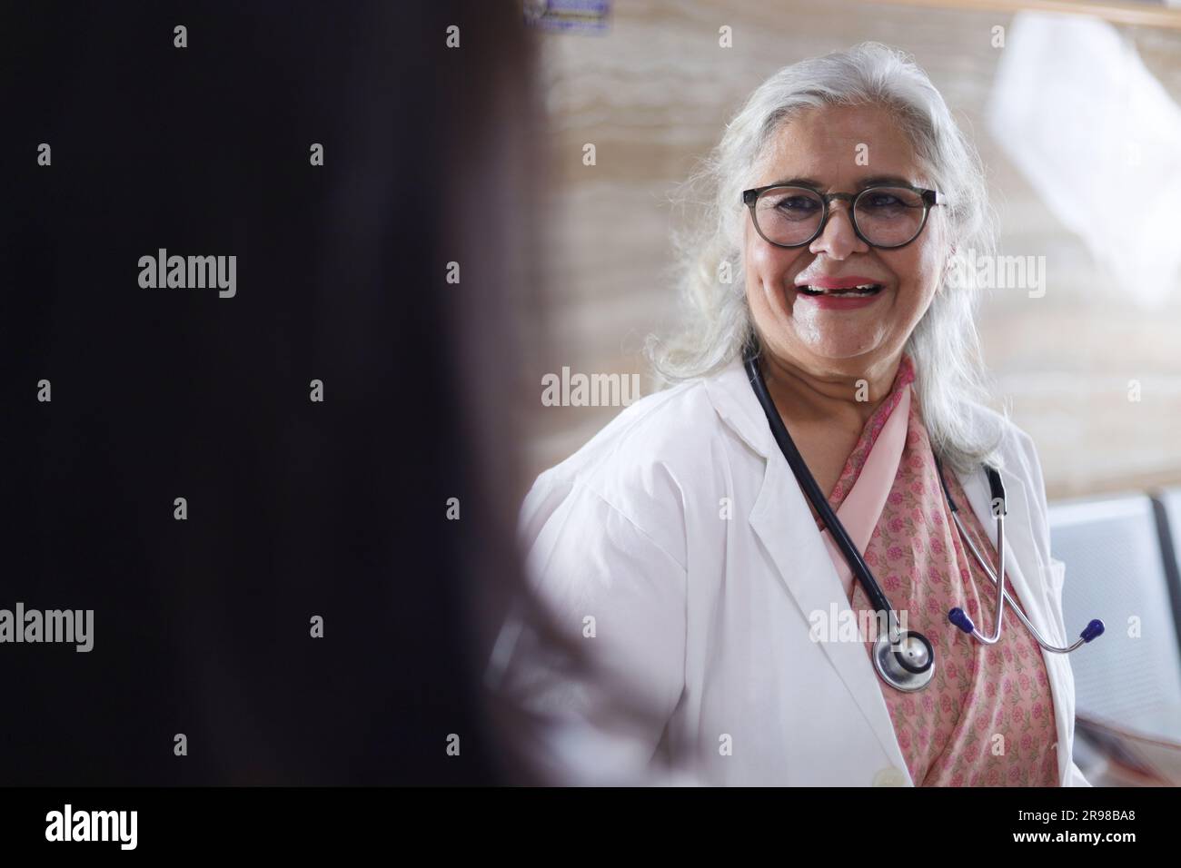 Médecin indien en discussion avec son assistant. Les médecins rient et parlent dans le couloir. Femme médecin âgée et jeune médecin. Médecin lisant le rapport du patient Banque D'Images