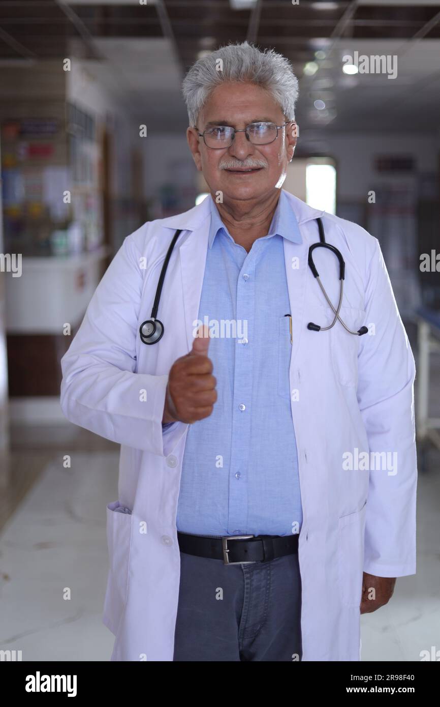 Portrait d'un médecin souriant en blouse de laboratoire montrant les pouces vers le haut. Heureux médecin senior en manteau blanc souriant sur fond de couloir d'hôpital. confiant. Banque D'Images