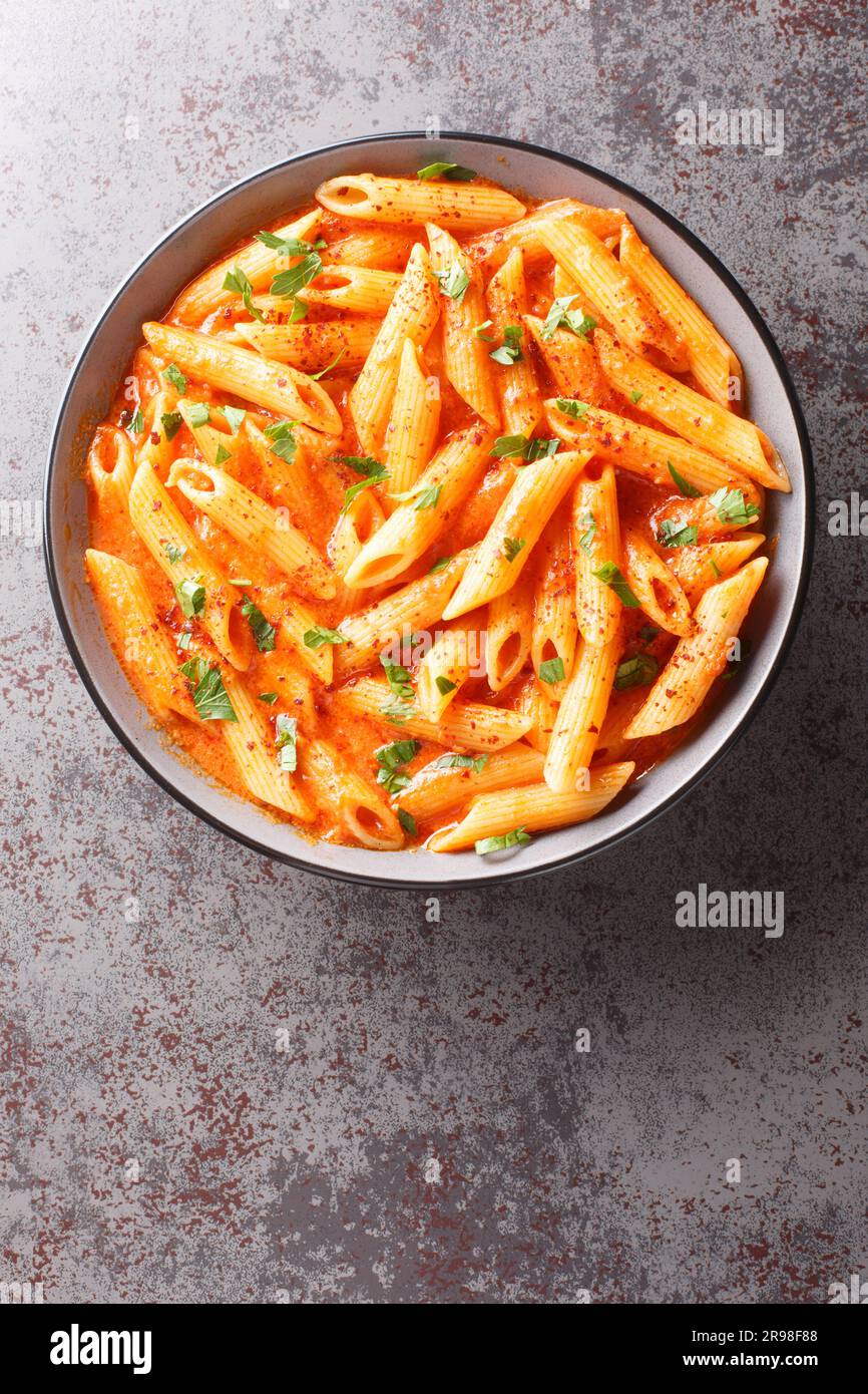 Délicieux beau bol de pâtes de penne dans la sauce tomate rose à côté du bol sur la table. Vue verticale du dessus Banque D'Images