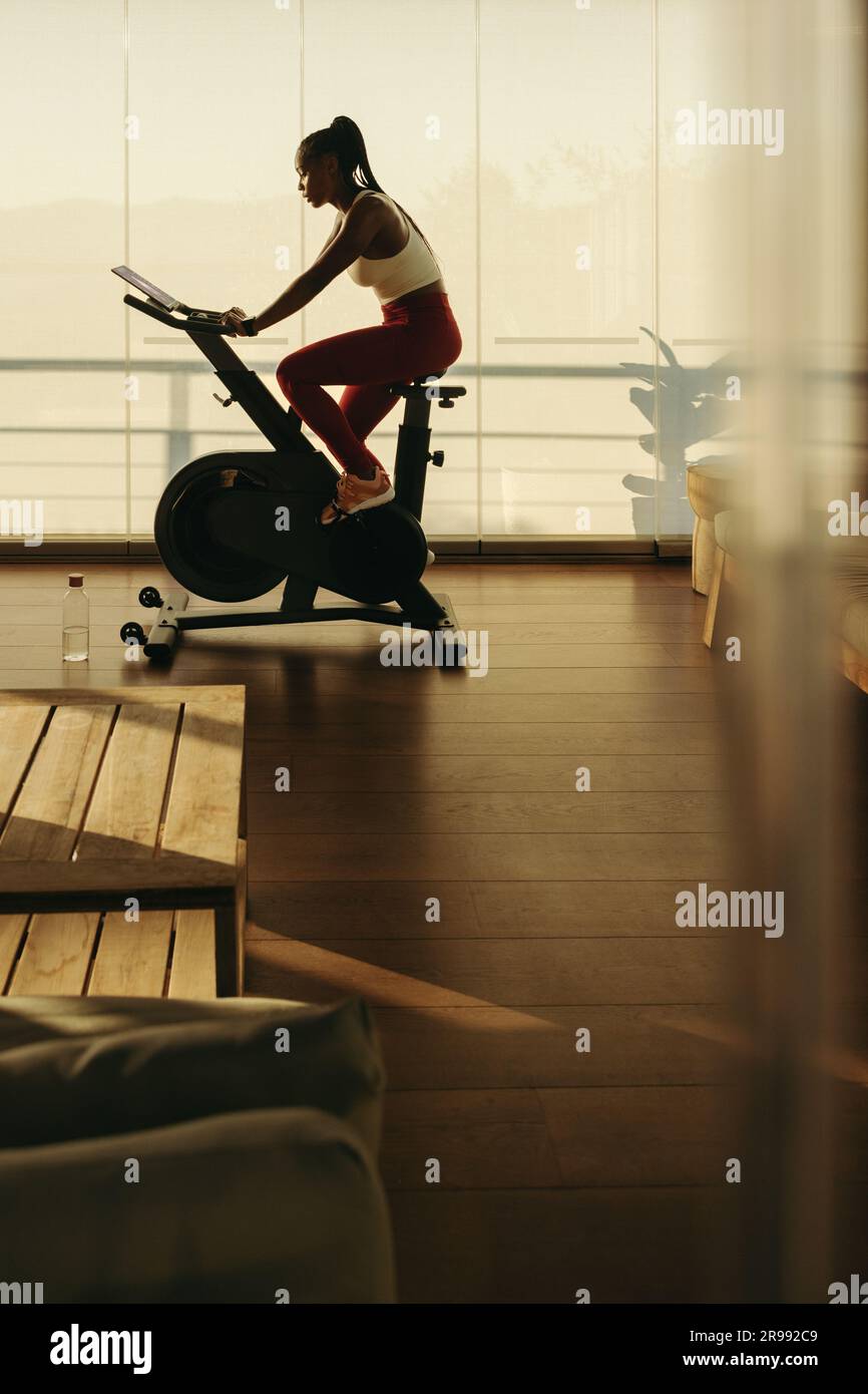 Une femme montre comment un vélo intelligent transforme la forme physique à la maison. Une athlète féminine s'entraîner à la maison avec facilité, atteignant ses objectifs de santé et de forme physique Banque D'Images