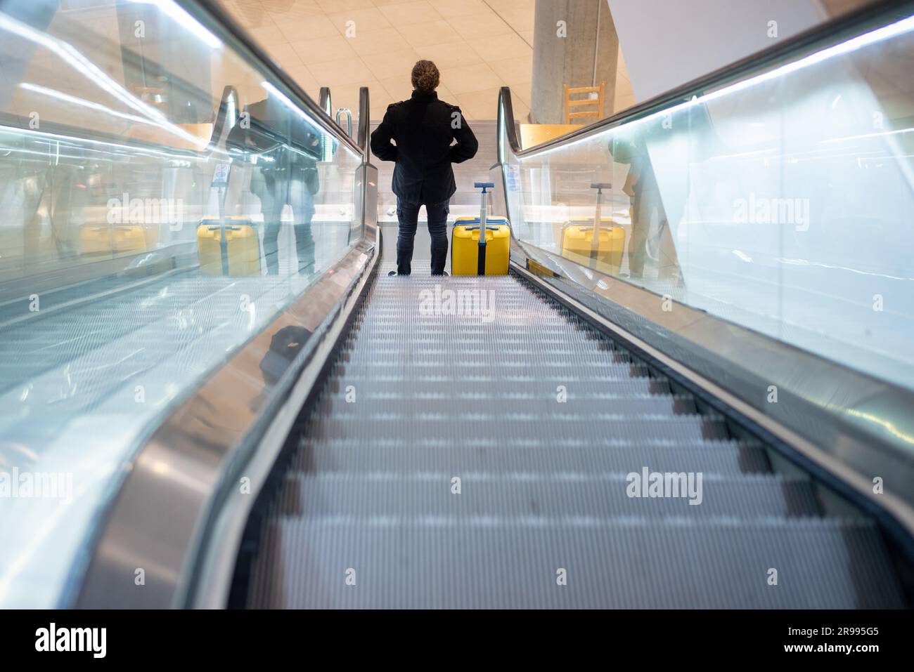 Touriste à l'aéroport avec une valise à roulettes sur l'escalier roulant Banque D'Images