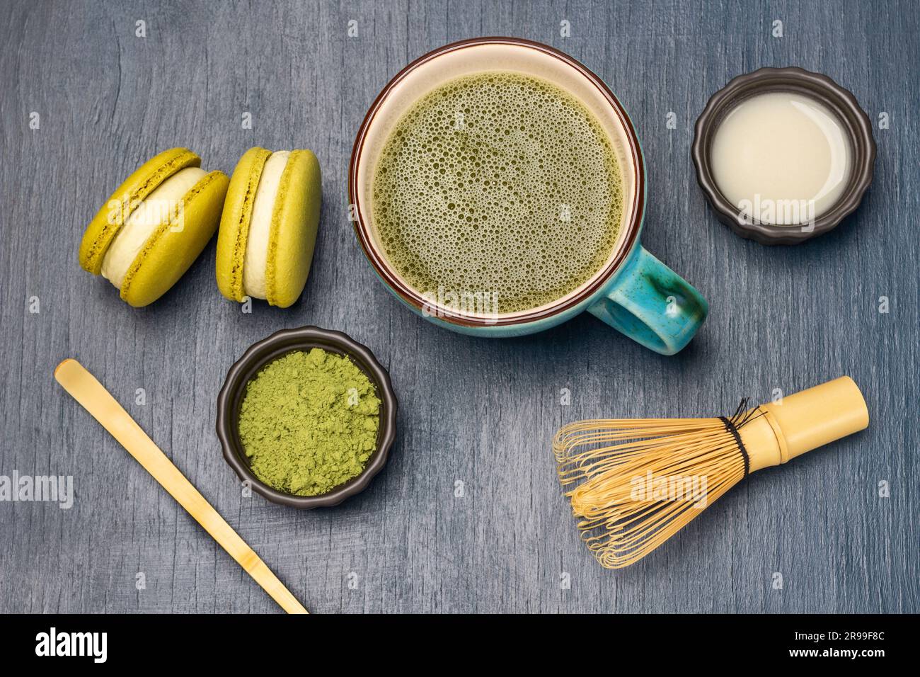 Cuillère de mesure et poudre de matcha verte. Lait dans un bol. Biscuits au macaron et thé au matcha dans une tasse. Pose à plat. Arrière-plan bleu Banque D'Images